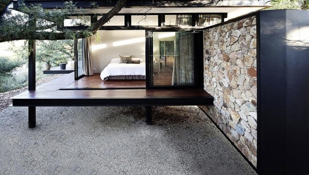 A bedroom opening through glass doors onto a dark timber deck beside a stone wall