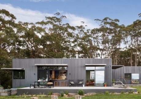 A dark clad single-storey cabin with a deep veranda and an outdoor kitchen